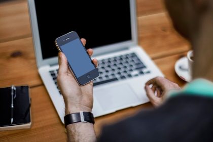 Person hält ein Smartphone vor einem Laptop – Symbolbild für die digitale Brieftasche d-you