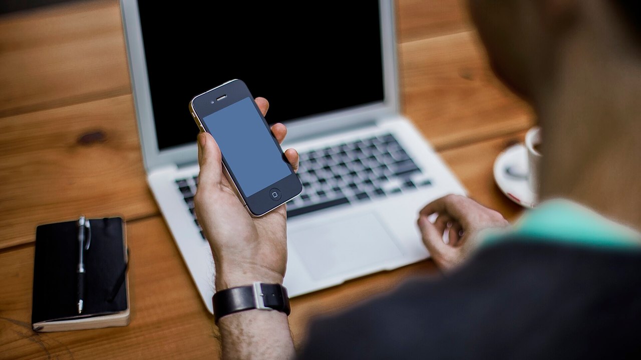 Person hält ein Smartphone vor einem Laptop – Symbolbild für die digitale Brieftasche d-you