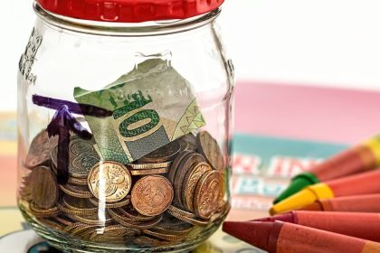 Sparglas mit Münzen neben Buntstiften als Symbol für die Frühstartrente für Kinder