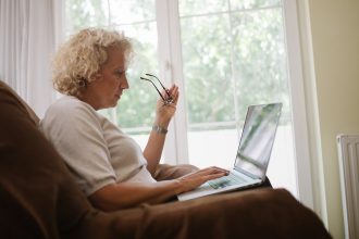 Ältere Frau sitzt im Sessel und arbeitet am Laptop