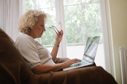 Ältere Frau sitzt im Sessel und arbeitet am Laptop