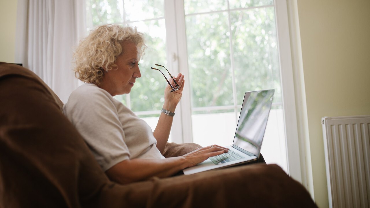 Ältere Frau sitzt im Sessel und arbeitet am Laptop