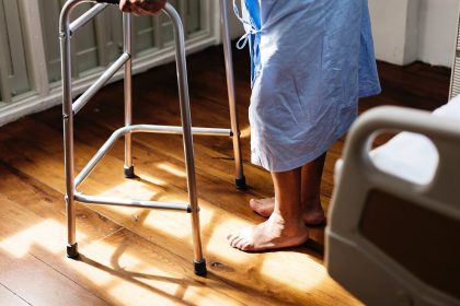 Person mit Gehhilfe neben einem Pflegebett