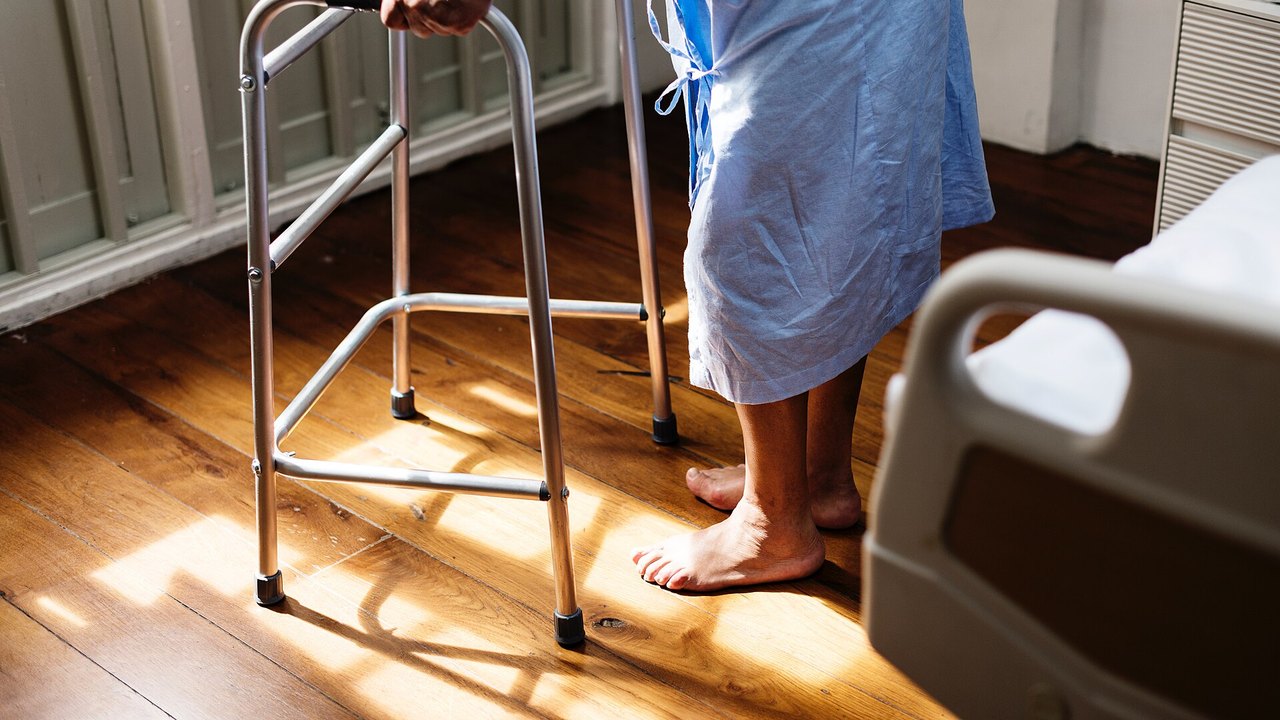 Person mit Gehhilfe neben einem Pflegebett